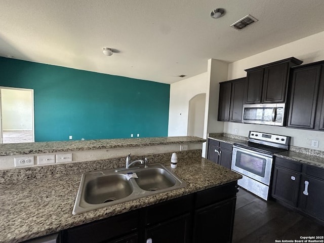 kitchen featuring stainless steel appliances, dark wood-type flooring, a sink, arched walkways, and visible vents