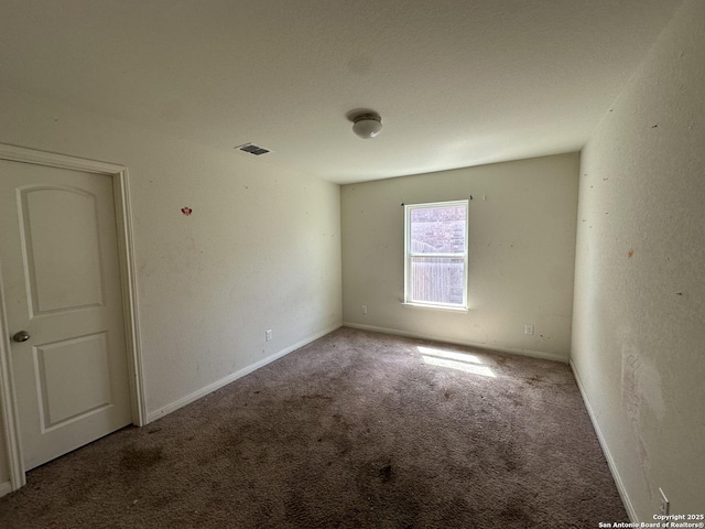 empty room featuring baseboards, visible vents, carpet floors, and a textured wall