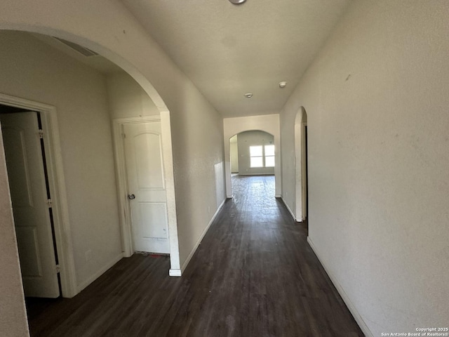 corridor featuring arched walkways, baseboards, and dark wood finished floors