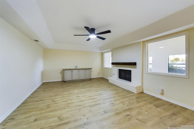 unfurnished living room with baseboards, light wood-style flooring, a ceiling fan, and a brick fireplace