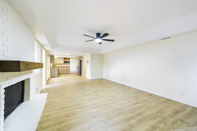 unfurnished living room featuring a ceiling fan, a tray ceiling, light wood-style floors, and baseboards