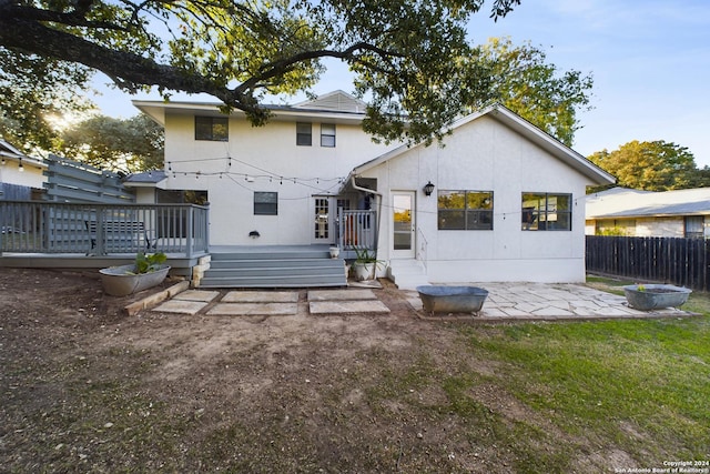 rear view of house with fence, a wooden deck, a patio, stucco siding, and a yard