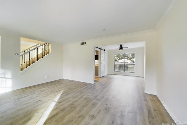 unfurnished living room featuring crown molding, stairway, a barn door, light wood-style flooring, and visible vents
