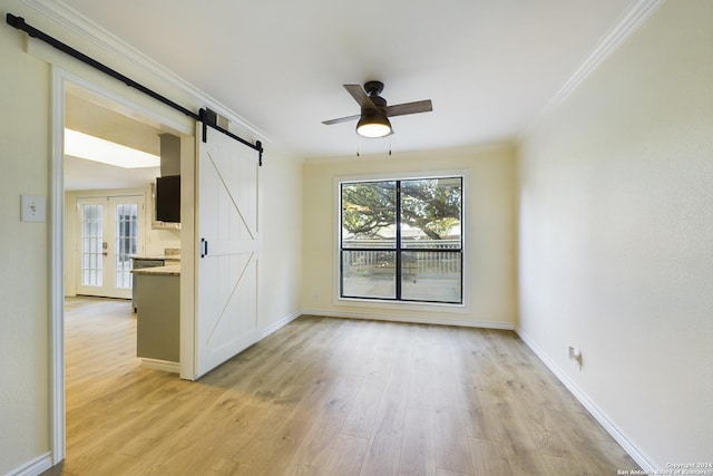 unfurnished room featuring a ceiling fan, light wood finished floors, a barn door, baseboards, and ornamental molding