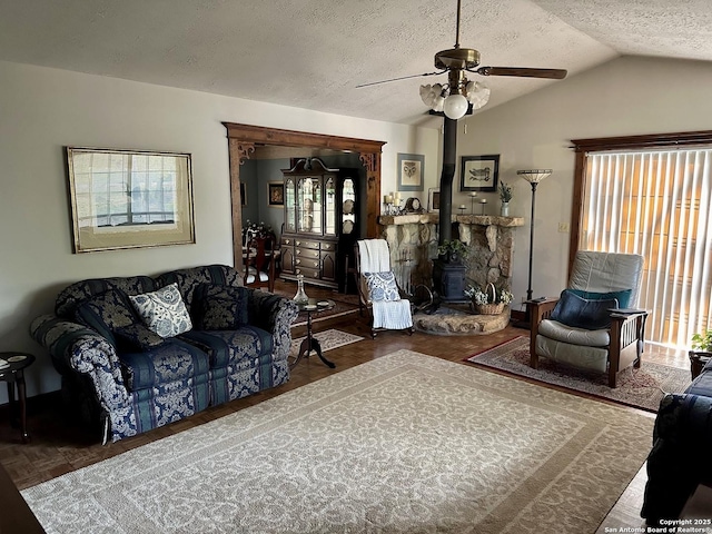 living room featuring a textured ceiling, lofted ceiling, ceiling fan, and a wood stove
