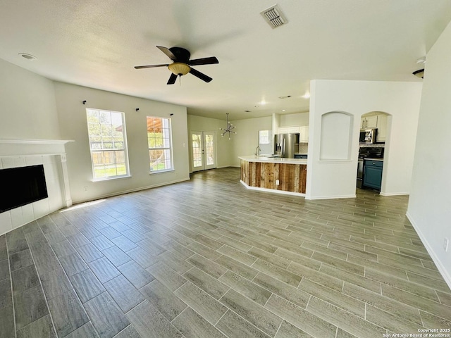 1064 Maltese Ln, San Antonio, TX 78260 - unfurnished living room with wood finish floors, ceiling fan with notable chandelier, baseboards, visible vents, and a tiled fireplace