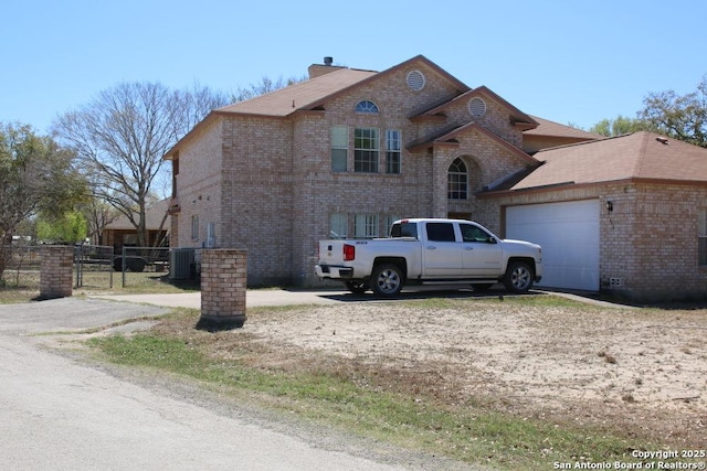 view of front facade with fence, a garage, driveway, brick siding, and central AC