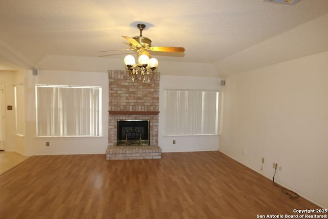 unfurnished living room featuring vaulted ceiling, a ceiling fan, wood finished floors, a textured ceiling, and a brick fireplace