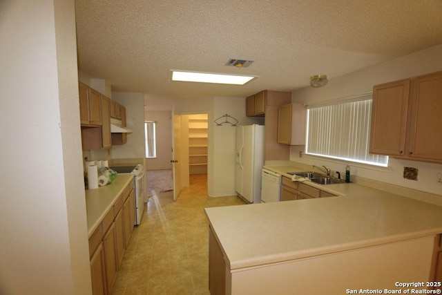 kitchen featuring white appliances, under cabinet range hood, a sink, visible vents, and a peninsula