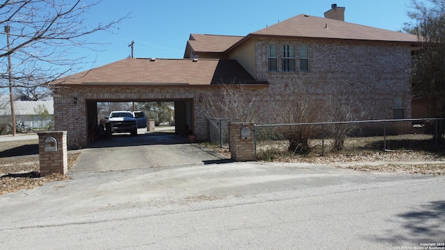 view of side of home with brick siding, a fenced front yard, a chimney, and concrete driveway