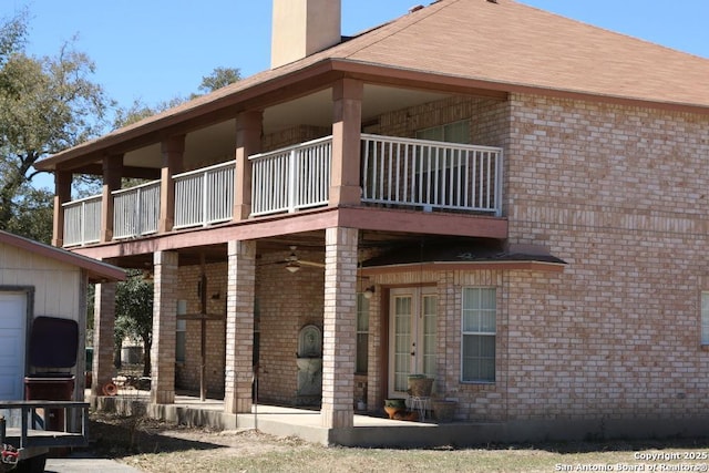 back of house with brick siding, a balcony, and a chimney