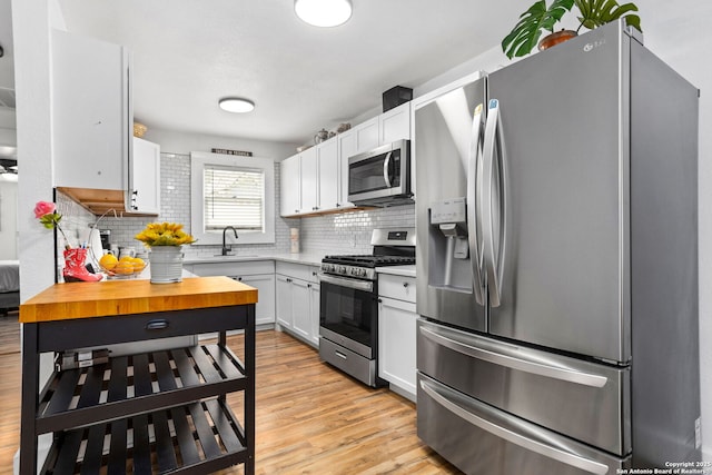 314 Trail, San Antonio, TX 78212 - kitchen with decorative backsplash, appliances with stainless steel finishes, white cabinetry, a sink, and light wood-style floors