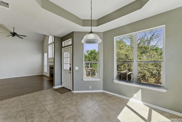 unfurnished dining area with ceiling fan, a glass covered fireplace, visible vents, tile patterned floors, and baseboards