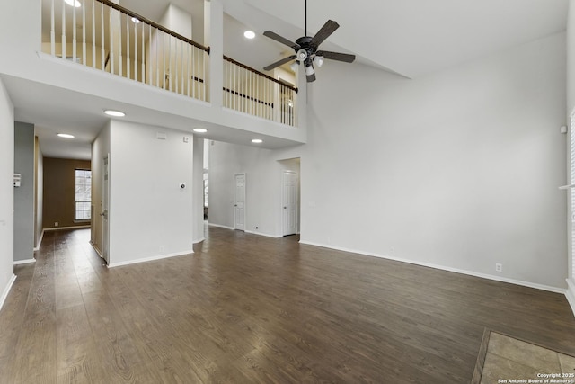 unfurnished living room featuring ceiling fan, a high ceiling, baseboards, and dark wood-style floors