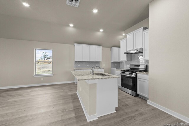 kitchen featuring under cabinet range hood, stainless steel gas stove, visible vents, a sink, and a kitchen island with sink