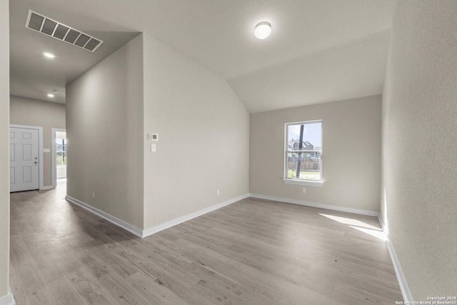 spare room featuring light wood-type flooring, baseboards, vaulted ceiling, and visible vents