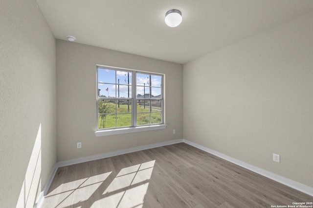 spare room with baseboards and wood finished floors