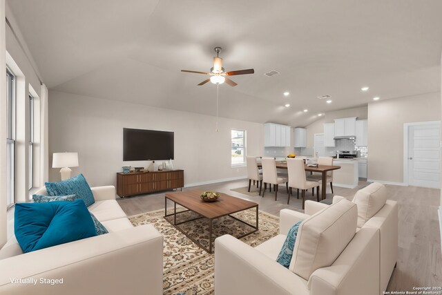 living area featuring vaulted ceiling, visible vents, light wood-style floors, and a ceiling fan