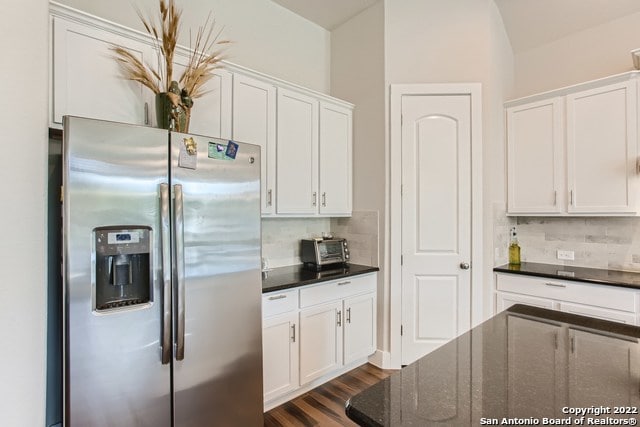 kitchen with white cabinetry, stainless steel refrigerator with ice dispenser, dark stone counters, backsplash, and dark wood-style floors