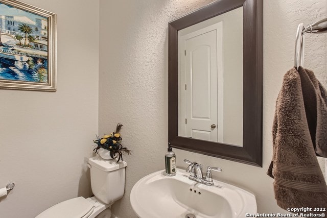 half bath with a textured wall, a sink, and toilet