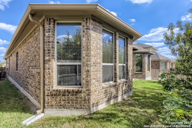 view of side of property featuring brick siding, fence, and a yard