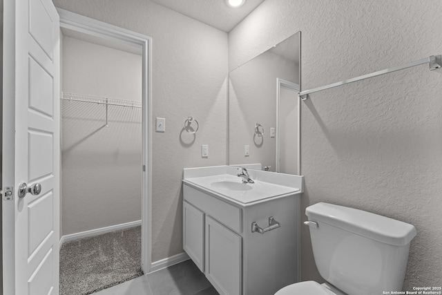bathroom featuring toilet, a textured wall, a walk in closet, and vanity