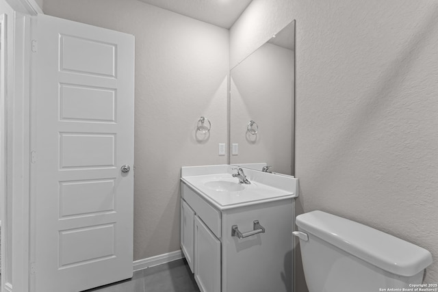 half bath featuring toilet, a textured wall, and vanity
