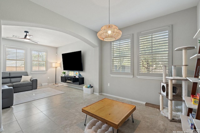 tiled living room featuring arched walkways, baseboards, and a ceiling fan