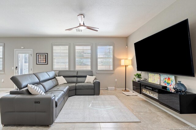 living area featuring visible vents, a glass covered fireplace, baseboards, and ceiling fan