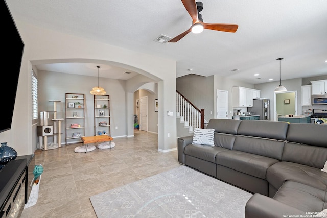 living room featuring visible vents, baseboards, stairway, a ceiling fan, and arched walkways