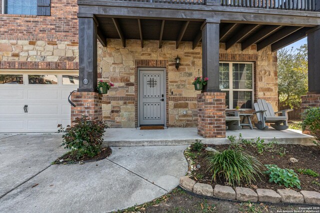 doorway to property featuring stone siding, an attached garage, and a porch