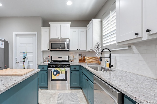 kitchen with stainless steel appliances, blue cabinets, a sink, white cabinets, and light stone countertops