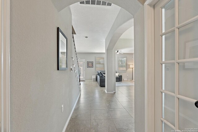 hall featuring tile patterned floors, arched walkways, baseboards, and visible vents