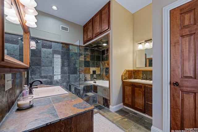 full bathroom featuring a relaxing tiled tub, stone tile flooring, baseboards, visible vents, and vanity