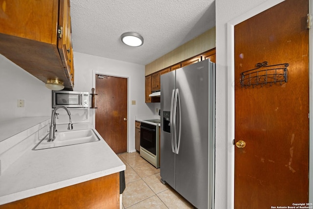 kitchen with light tile patterned floors, light countertops, under cabinet range hood, appliances with stainless steel finishes, and a sink
