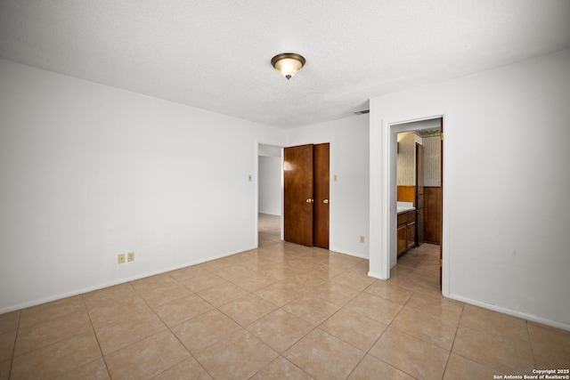 empty room featuring light tile patterned floors, a textured ceiling, and baseboards