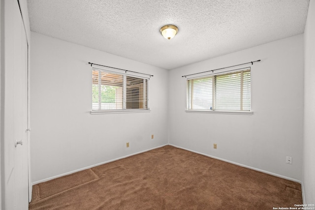 carpeted empty room with a textured ceiling, a healthy amount of sunlight, and baseboards