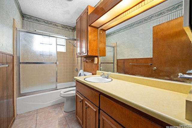 bathroom featuring wallpapered walls, tile patterned flooring, a textured ceiling, toilet, and wainscoting
