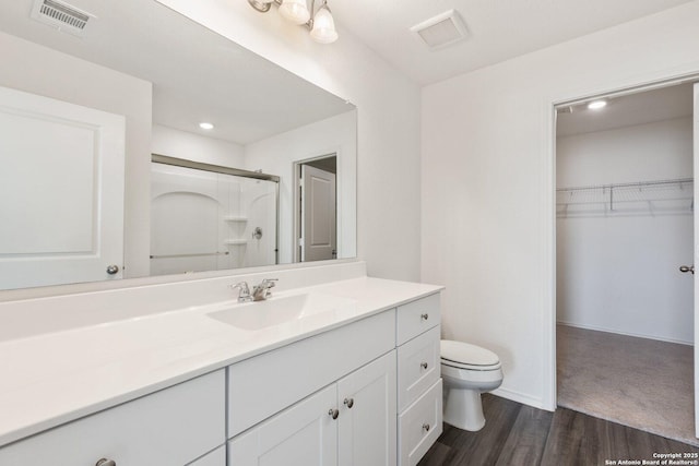 bathroom with toilet, vanity, a shower with door, and visible vents