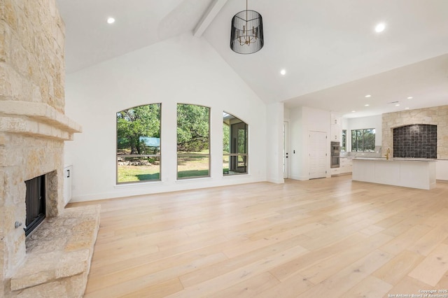 unfurnished living room featuring high vaulted ceiling, beamed ceiling, a stone fireplace, and light wood finished floors