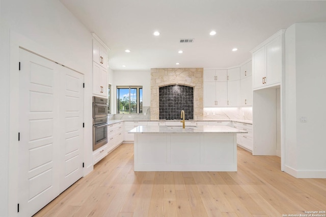 kitchen with light wood-type flooring, visible vents, a sink, and tasteful backsplash