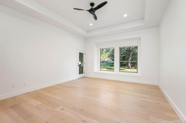 spare room with ceiling fan, baseboards, a raised ceiling, and light wood-type flooring