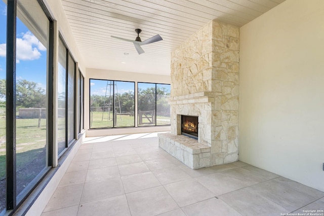 unfurnished living room with wood ceiling, light tile patterned floors, ceiling fan, and a stone fireplace