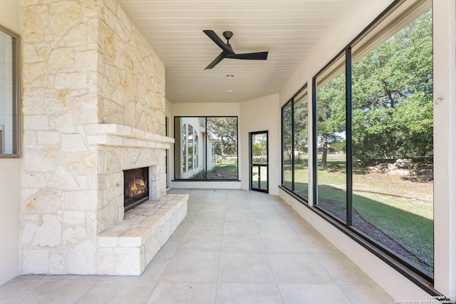 unfurnished sunroom featuring a stone fireplace and ceiling fan