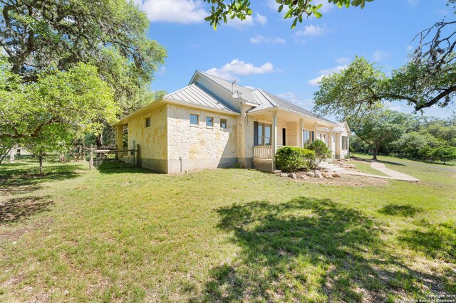 back of house featuring a yard, a standing seam roof, fence, metal roof, and stone siding