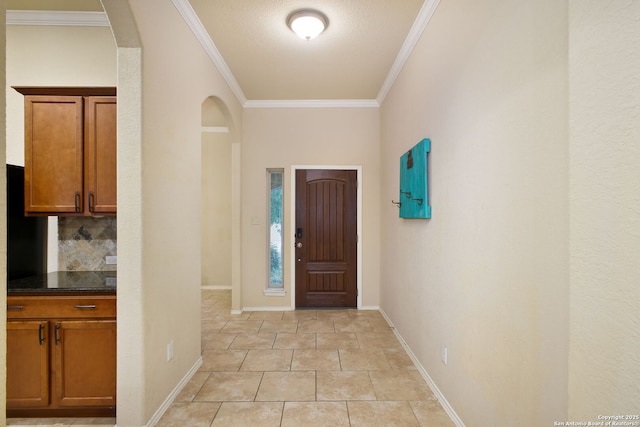 entrance foyer with crown molding, arched walkways, baseboards, and light tile patterned flooring