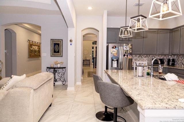 kitchen featuring stainless steel refrigerator with ice dispenser, marble finish floor, arched walkways, light stone counters, and visible vents
