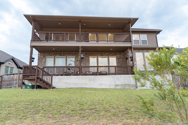 back of property with a balcony, a lawn, fence, and brick siding