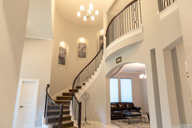 stairway with a high ceiling, arched walkways, ornamental molding, and a chandelier