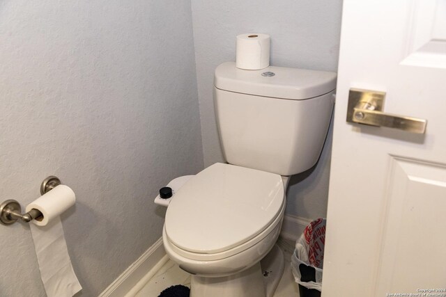 bathroom featuring toilet, a textured wall, and baseboards